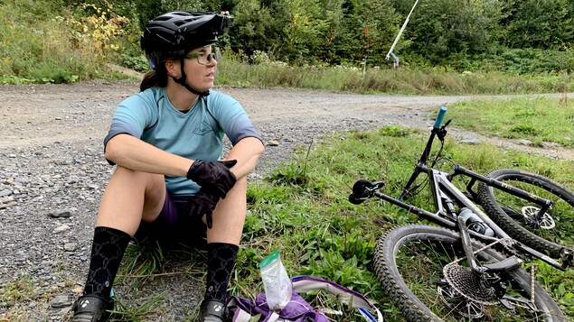 La cycliste Geneviève Simard est assise par terre sur le bord d'une route de gravier.