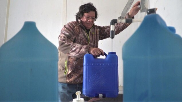 Une personne d'une communauté autochtone remplit un bidon d'eau potable.
