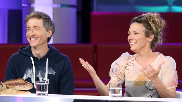 Un homme et une femme qui rient. Quelques pains sont posés sur la table devant l'homme.