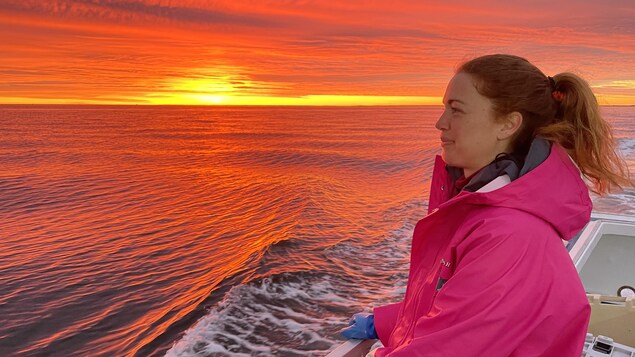 Une femme sur un bateau. Devant elle, un coucher de soleil.