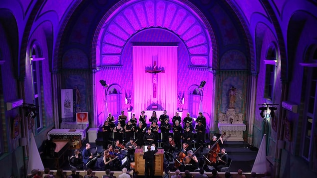 Un orchestre composé d'une trentaine de musiciens joue dans une église illuminée.
