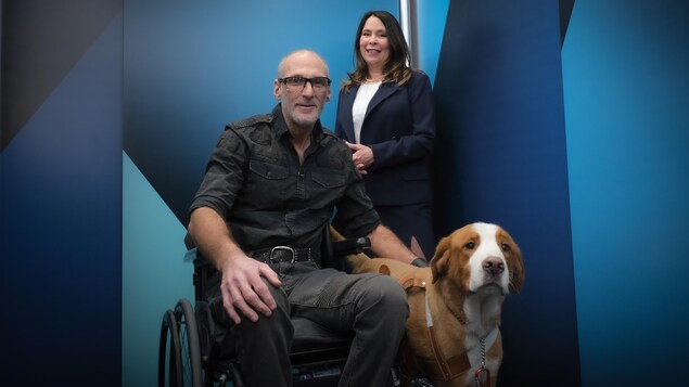 Un homme en fauteuil roulant et une femme sont accompagnés d'un chien.