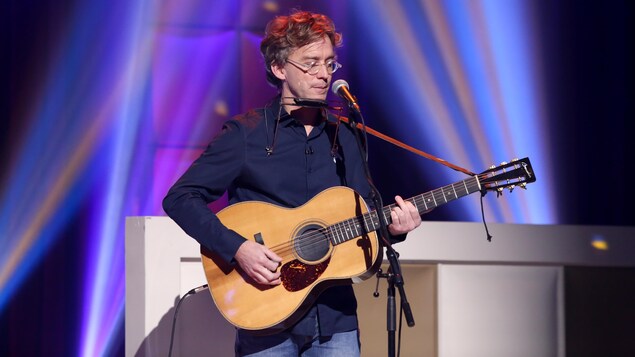 Fred Pellerin chante en s'accompagnant à la guitare.