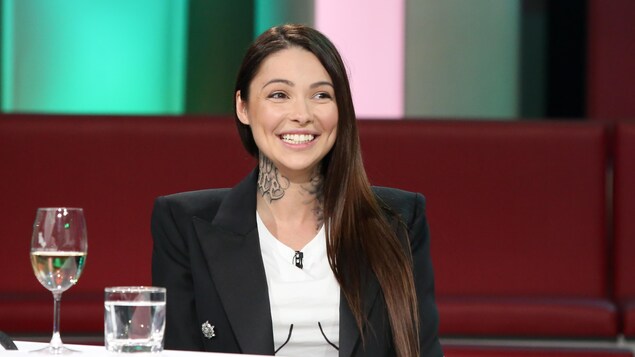 Une femme aux longs cheveux bruns. Elle a des tatouages sur le cou.