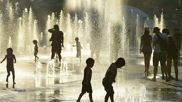 Des enfants s'amusent avec des jets d'eau au centre-ville de Montréal.