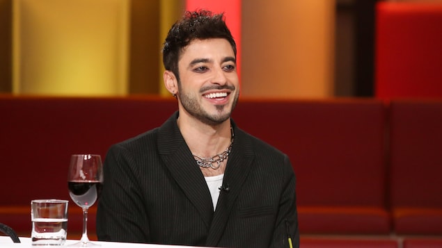 Jade Hassouné sourit. Il porte un t-shirt blanc et un veston noir.