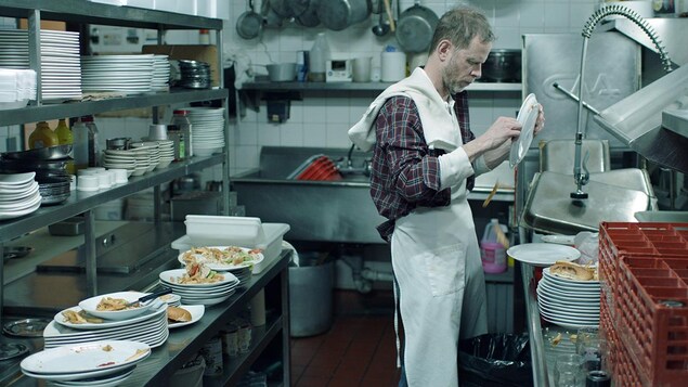 Un homme lave de la vaisselle dans une cuisine de restaurant.
