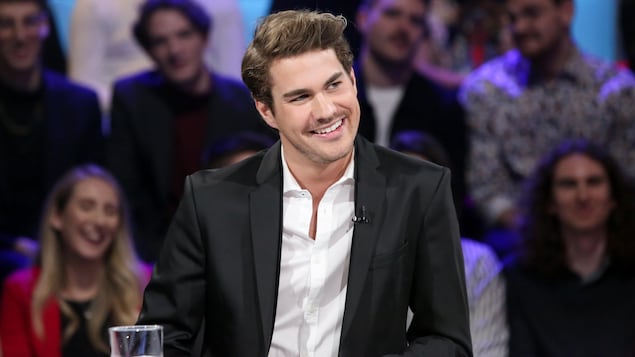 L'homme est assis à la table des invités d'un plateau de télévision.