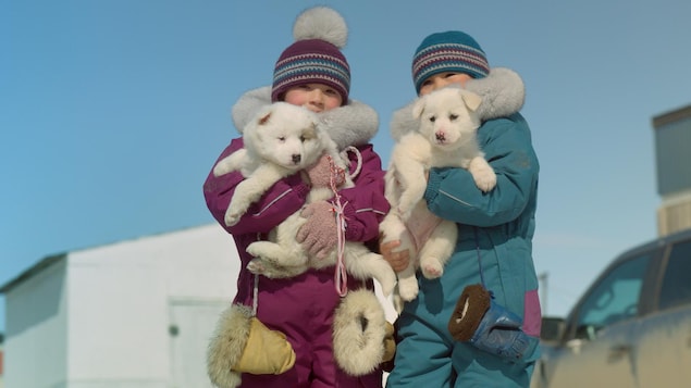 Deux enfants en habit de neige tiennent des chiots dans leurs bras.