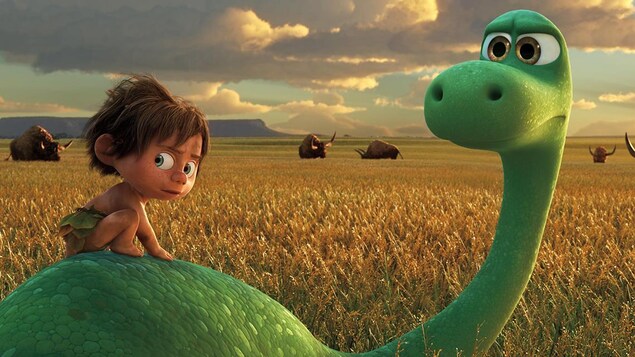 Un petit garçon sur le dos d'un dinosaure, tous deux face à des buffles.