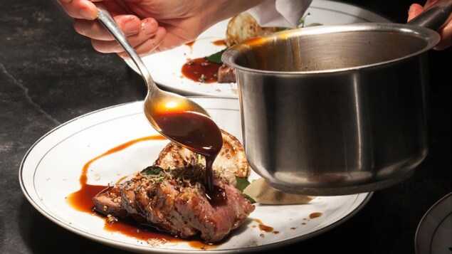 Un cuisinier qui dresse une assiette de boeuf avec de la sauce.