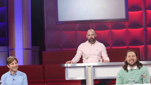 Trois hommes : le premier porte une chemise bleue, le deuxième un chandail rose et le troisième un chandail vert.