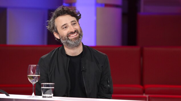 Un homme qui porte la barbe. Il sourit.