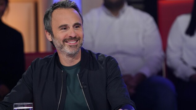 Un homme qui sourit. Il porte un chandail vert et un blouson noir.
