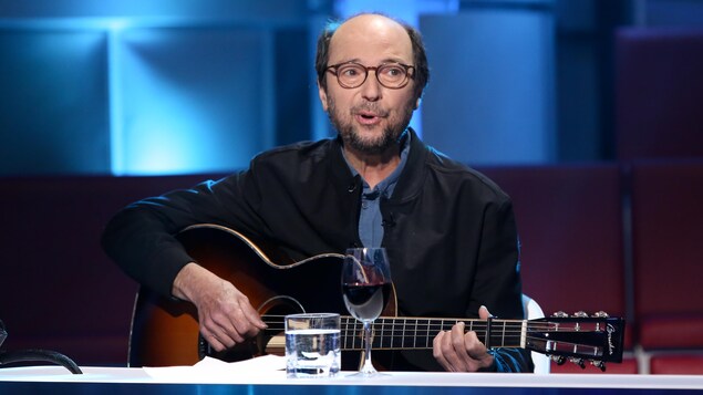 Michel Rivard chante et joue de la guitare.