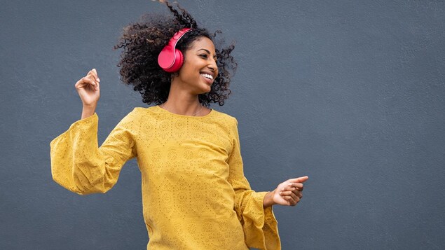 Une femme écoute de la musique en dansant. Elle porte des écouteurs sur ses oreilles.