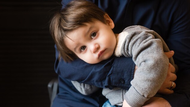 Un petit garçon à l'air inquiet ne semble pas vouloir quitter les bras de son papa.