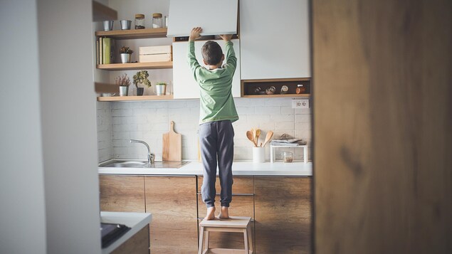 Un petit garçon seul à la maison fouille dans un placard de cuisine. 
