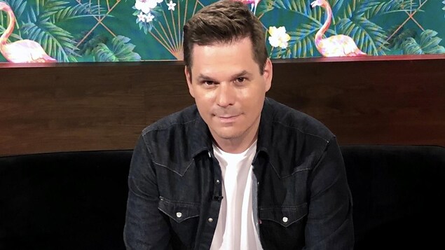 Portrait de l'homme qui est assis dans un studio de télévision et sourit en regardant devant lui.