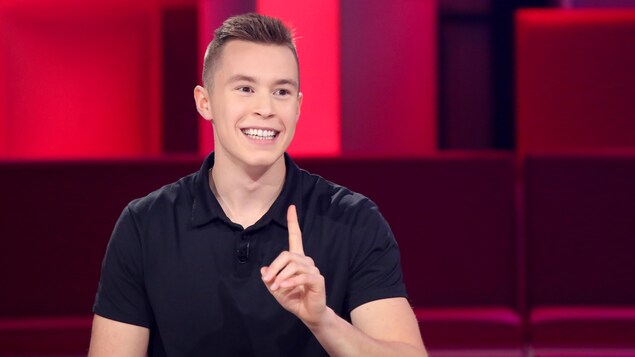 Raphaël Lessard est à la table des invités. Il porte un t-shirt bleu marine.