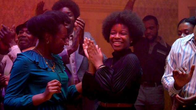 Un groupe d'hommes et de femmes noirs dansent et sourient, dans une pièce éclairée de rouge.