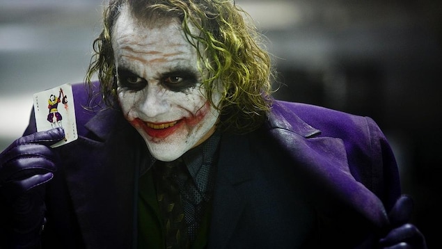 Un homme aux cheveux verts et au visage maquillé de blanc et de rouge brandit une carte de joker Un homme aux cheveux verts et au visage maquillé de blanc et de rouge brandit une carte de joker