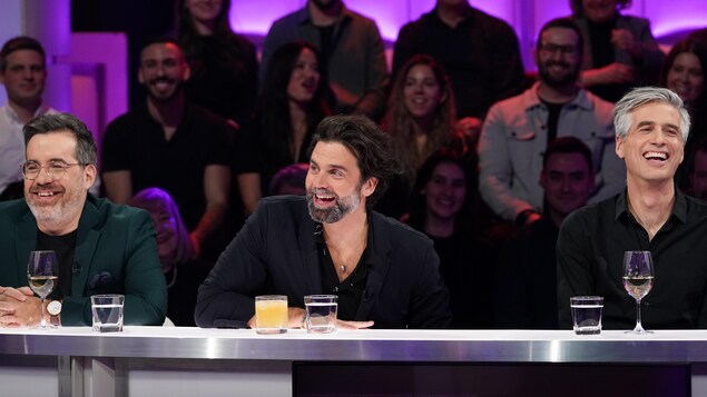 Le trio est assis en studio et rit.