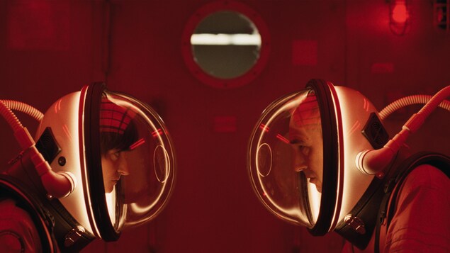 Dans un éclairage rouge, deux personnes portant un casque d'astronaute se font face.