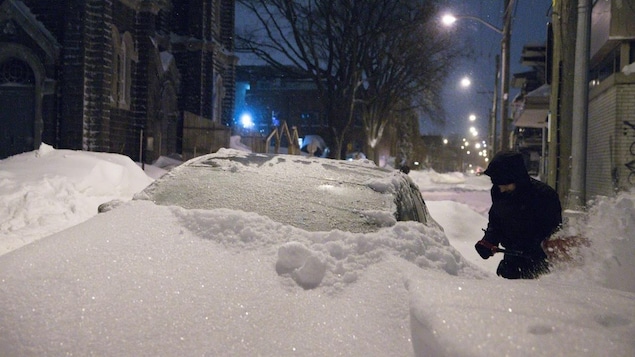 Un homme déneigeant sa voiture près de l'église St-Charles