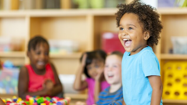 On voit quatre enfants de 4/5 ans sourire à la garderie.