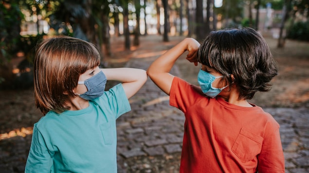 Deux enfants se saluent avec avec le coude et portent un masque.