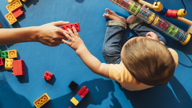 Un bébé, vu de haut, joue avec des blocs LEGO.