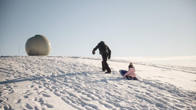 Un adulte tire un enfant sur une luge pour monter une cote.