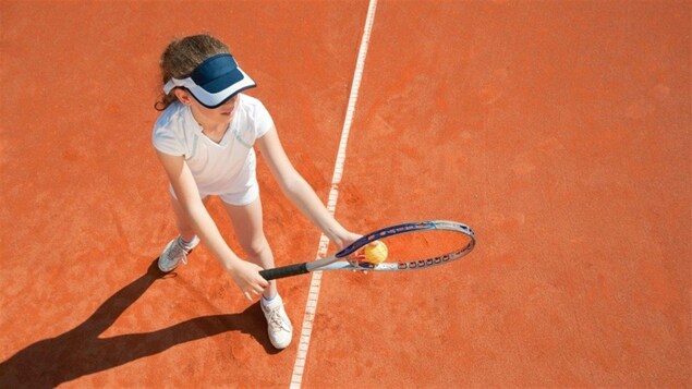 Une jeune fille se prépare à faire un service sur un court de tennis.