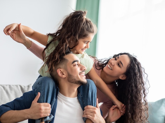 Le papa porte la fillette sur ses épaules et celle-ci sourit à sa maman. C'est une famille d'origine arabe ou perse. 