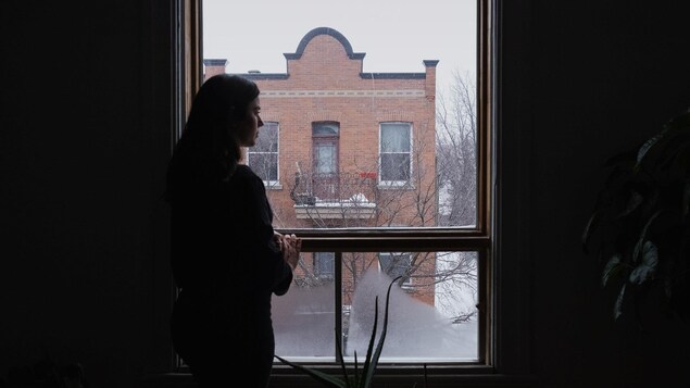 Une jeune dame regarde par la fenêtre de son appartement.