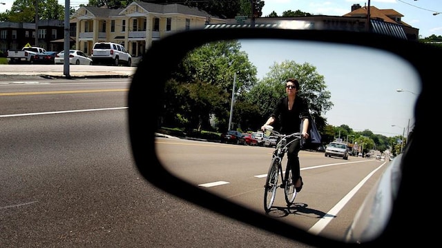 Un automobiliste voit une cycliste dans son rétroviseur.