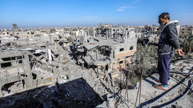 Un homme se tient sur un plateau surplombant une ville dont de nombreux immeubles sont en ruines.