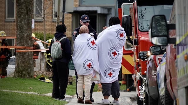 À l'extérieur, deux femmes enveloppées de couvertures de la Croix-Rouge discutent avec un employé du service d'incendie.