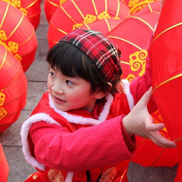 طفلة ذات ملامح شرق آسيوية ترفع كرة هوائية حمراء اللون.