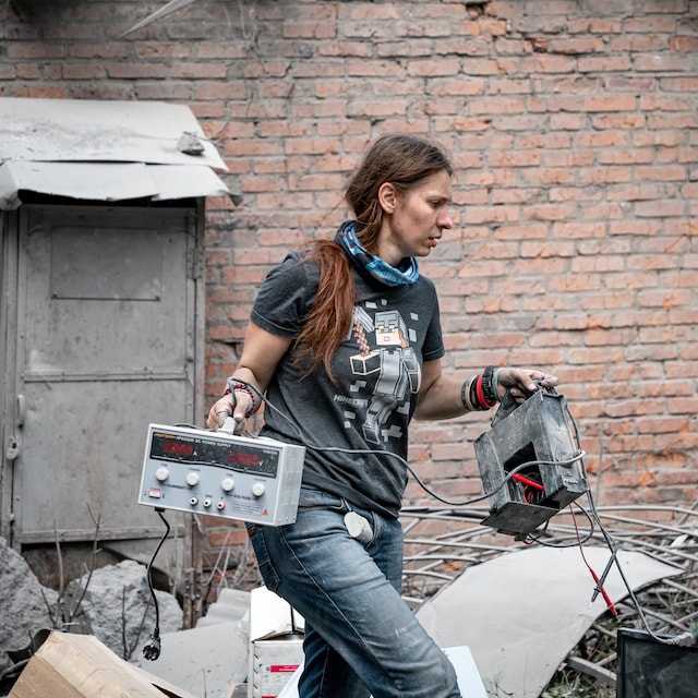 Kseniia Minakova marche au milieu de décombres avec des appareils scientifiques électroniques dans les mains.