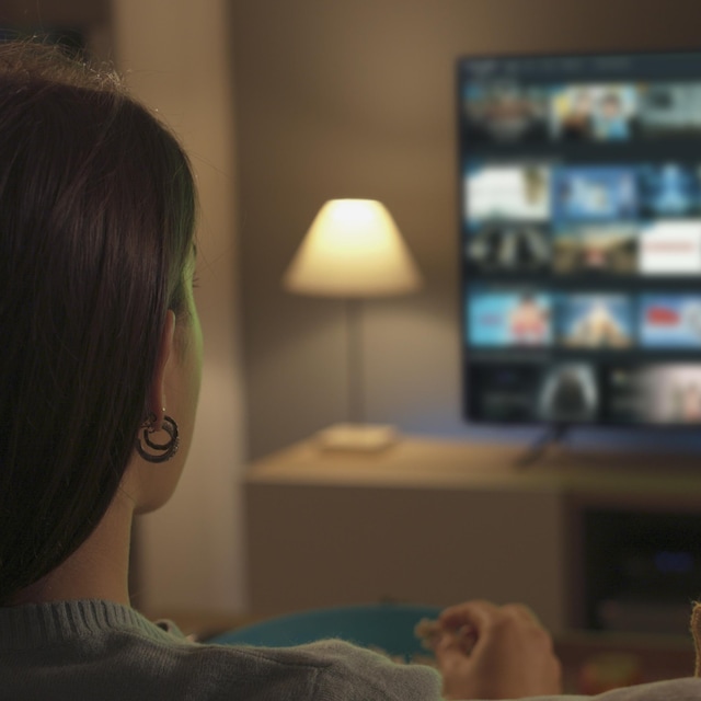 Une femme assise dans un salon qui regarde une télévision où l'on peut voir une sélection de contenus dans une plateforme de diffusion en continu.