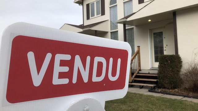 Une pancarte indiquant Vendu; à l'arrière-plan, une maison de banlieue.