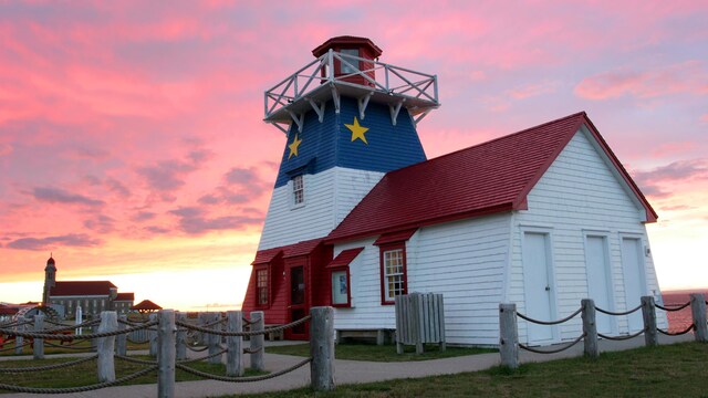 Un phare composé d'une maison et de la tour. C'est à l'heure du coucher du soleil. 