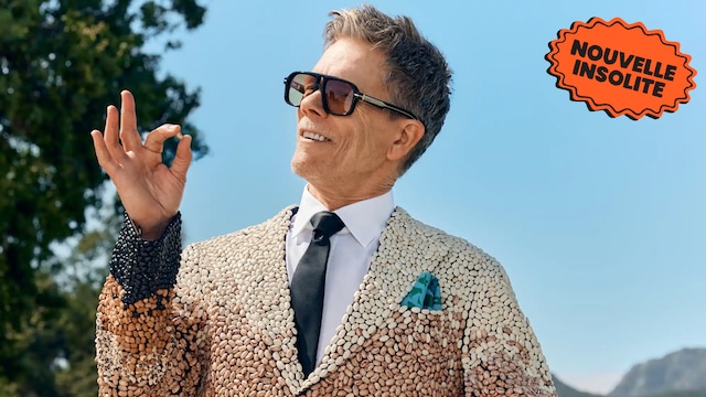 L'acteur Kevin Bacon sourit en portant un gilet fait entièrement d'haricots en inspectant un haricot dans ses doigts.