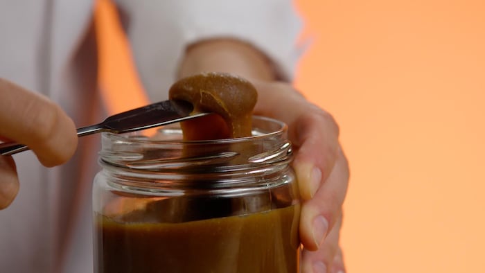 Un couteau rempli de caramel au dessus d'un pot en verre. 