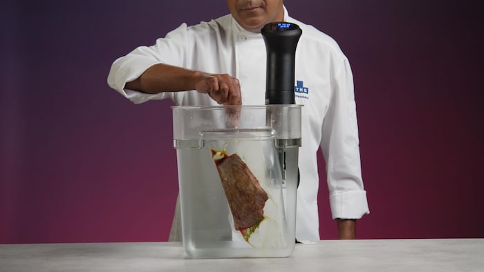 Un main qui dépose un morceau de viande emballée dans un contenant rempli d'eau.