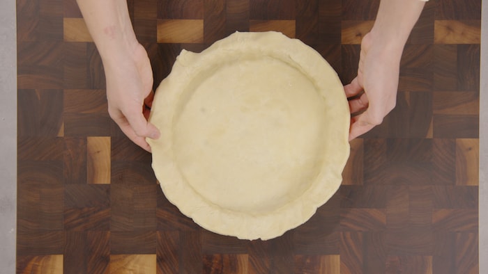 Une personne étend doucement de la pâte dans un moule à tartre. 