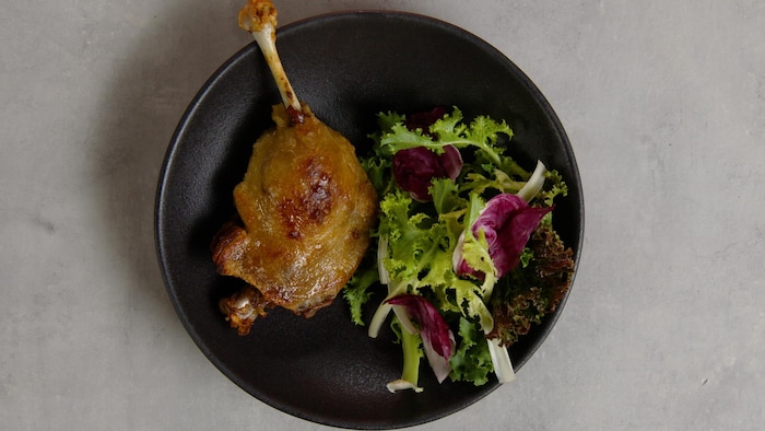 Cuisse de canard confit accompagnée d'une salade verte dans une assiette.