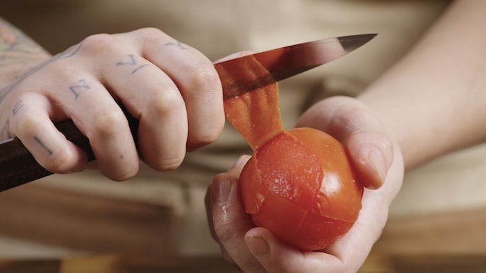 Une personne a une main un petit couteau et une tomate italienne. 